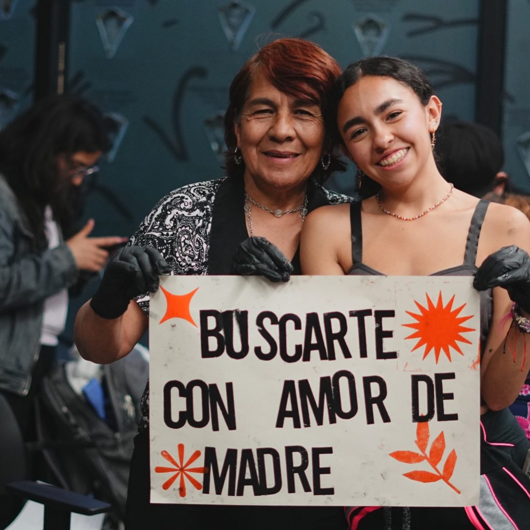 Mujer mayor con mujer joven, juntas sosteninendo cartel 